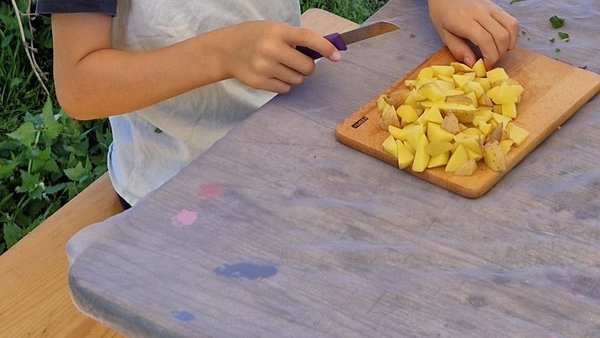 Kind schneidet Kartoffeln am Tisch.